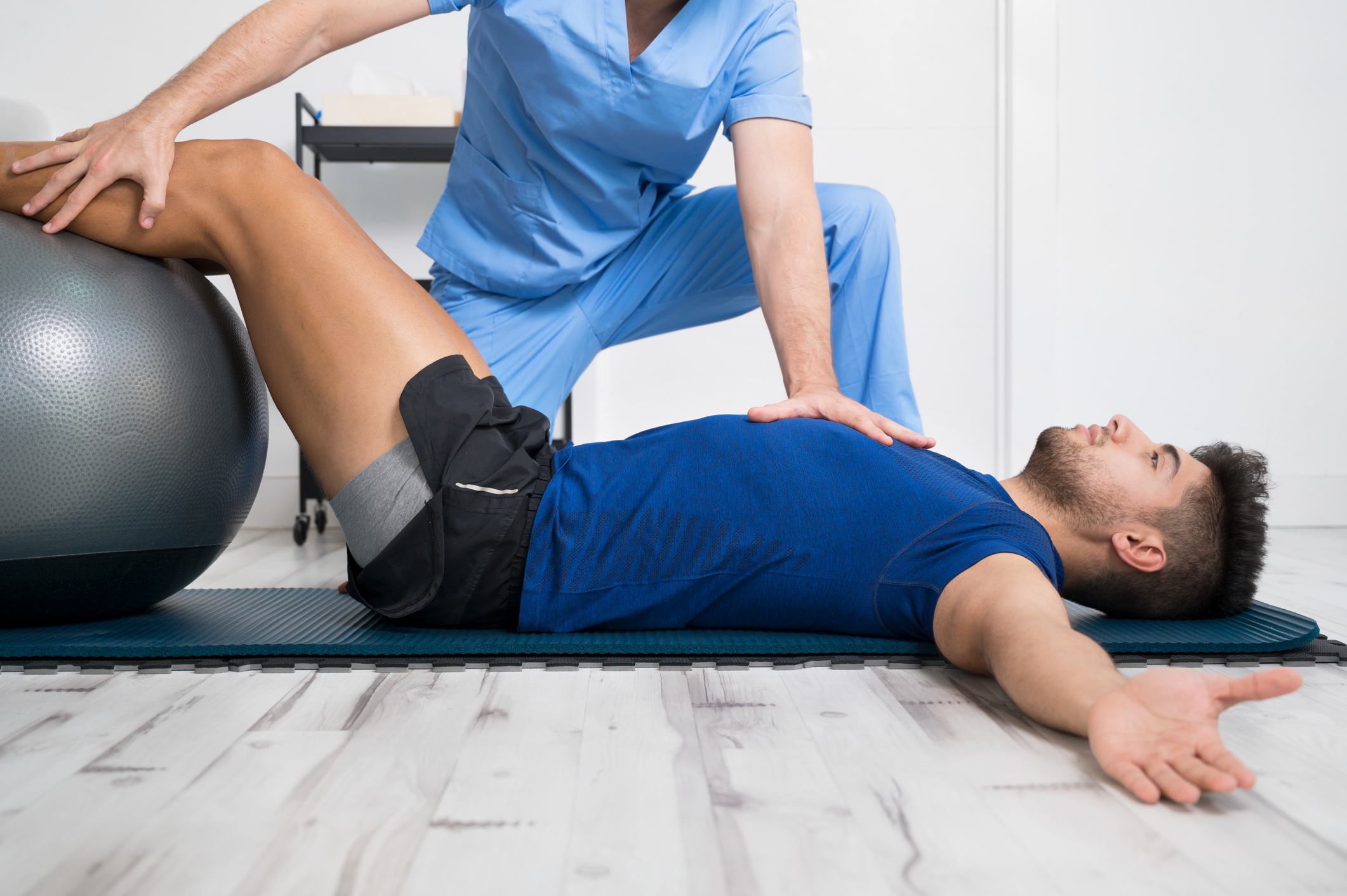 Fisioterapeuta con paciente tumbado sobre colchoneta y sus piernas sobre una pelota